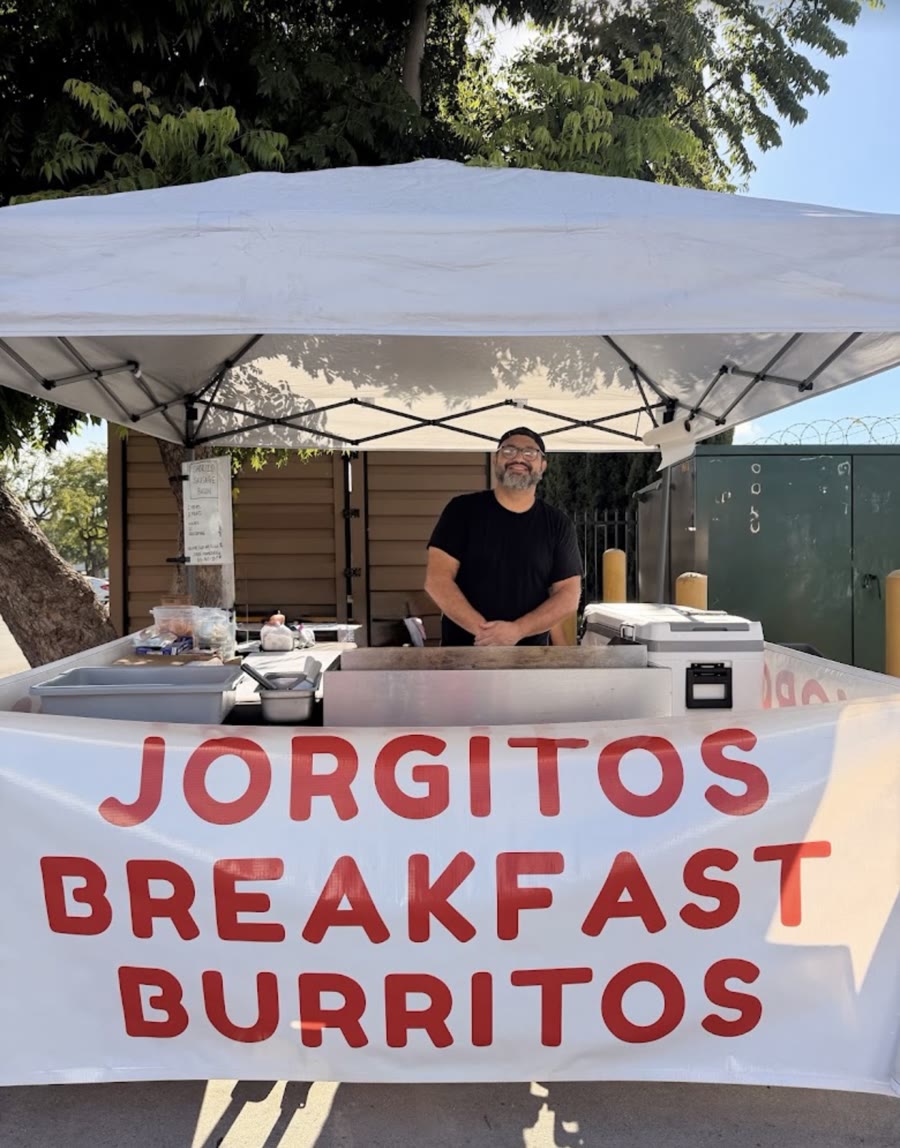 Jorge smiling behind the griddle under the white tent, with the Jorgitos Breakfast Burritos banner in front
